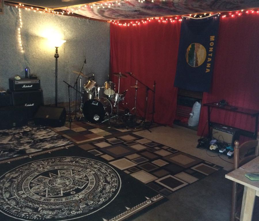 A home recording studio with a drum kit, microphones, amplifiers, acoustic treatment, and rugs